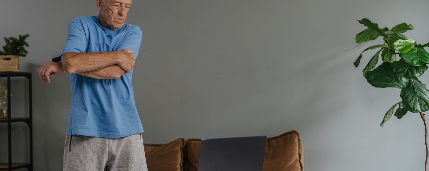 A man in a blue shirt stretching one arm across his chest at home