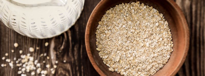 A wooden bowl of raw rolled oats on a dark table