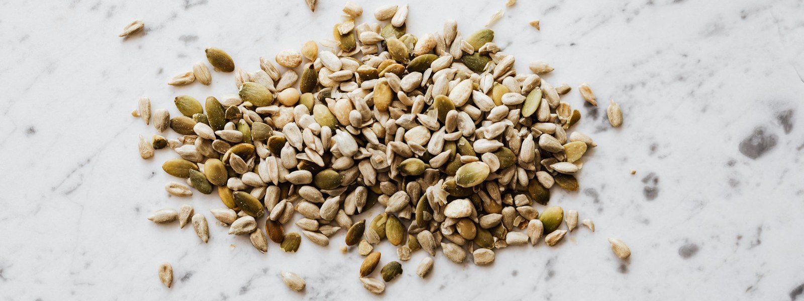 A pile of pumpkin and sunflower seeds on a white marble surface