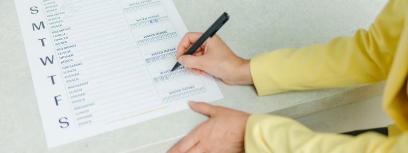 A hand filling in a weekly meal and symptom tracking sheet