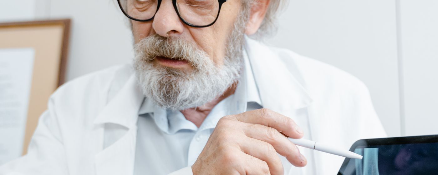 A senior doctor in a white coat reviewing an image on a digital tablet in a clinic