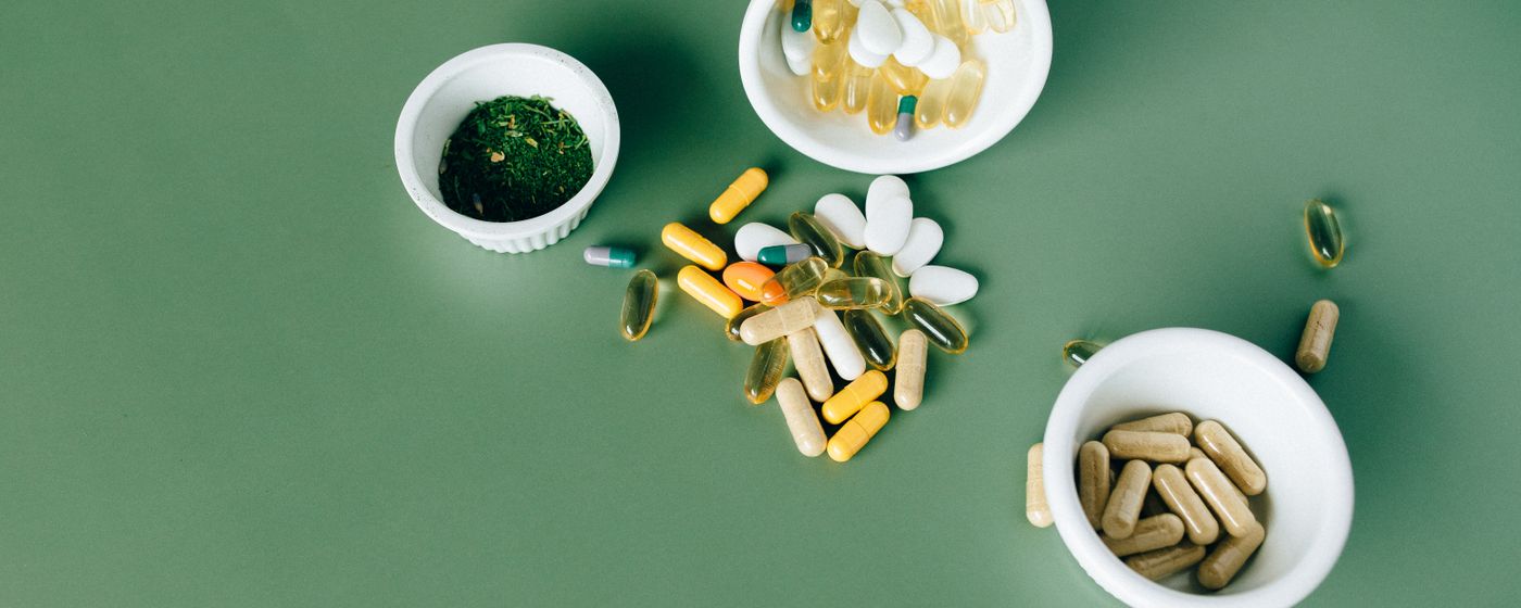 Assorted vitamin capsules and tablets in small bowls on a green surface.