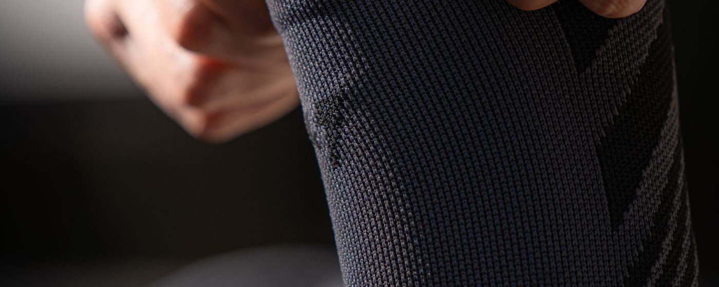 A close-up of a person pulling a dark knitted compression sock up the calf