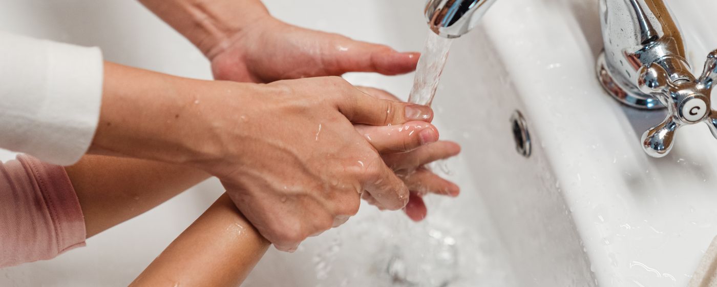 A person washing their hands under running water at a white sink