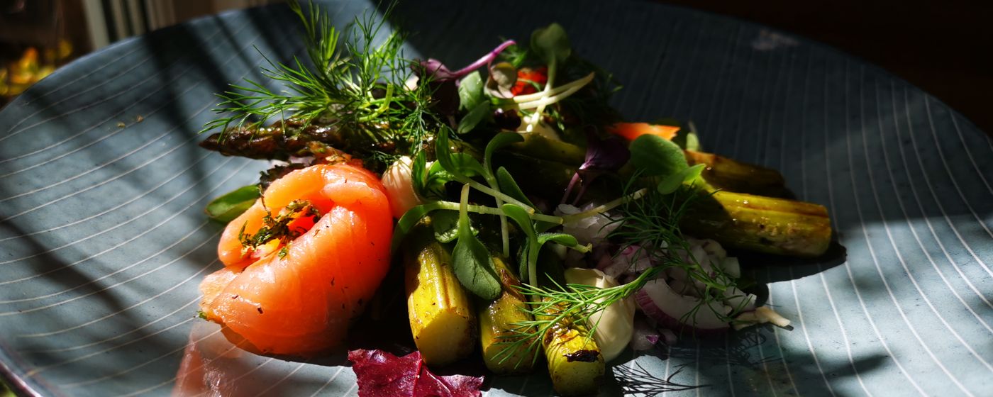 A dark plate of salad with tomatoes, leafy greens and herbs