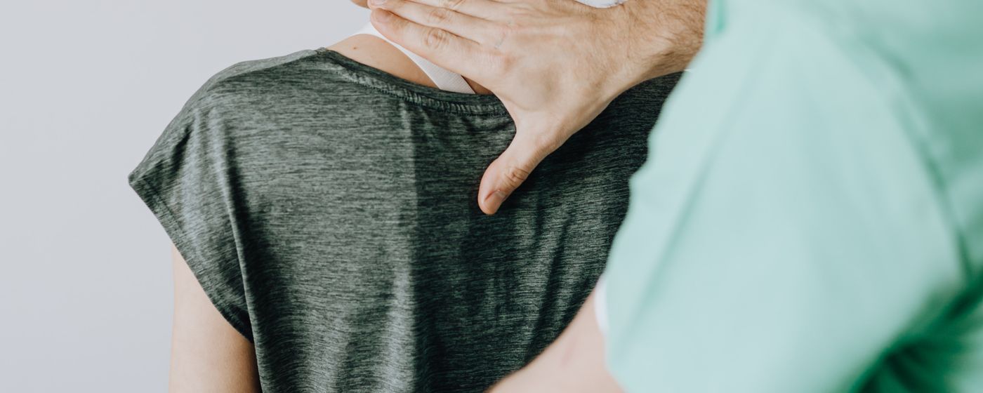 A clinician's hand resting on the back of a person in a grey top during a hands on therapy session