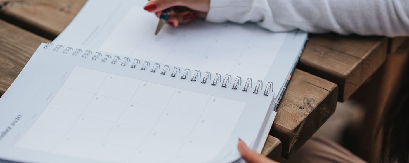A hand writing in an open monthly planner resting on a wooden bench