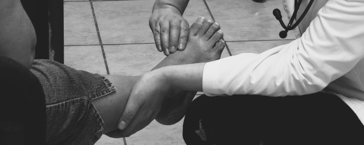 A clinician examining a patient's bare foot and ankle in a clinic