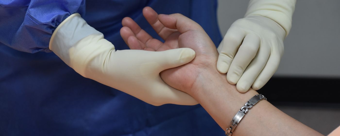 A clinician wearing gloves holding a patient's wrist to take a pulse