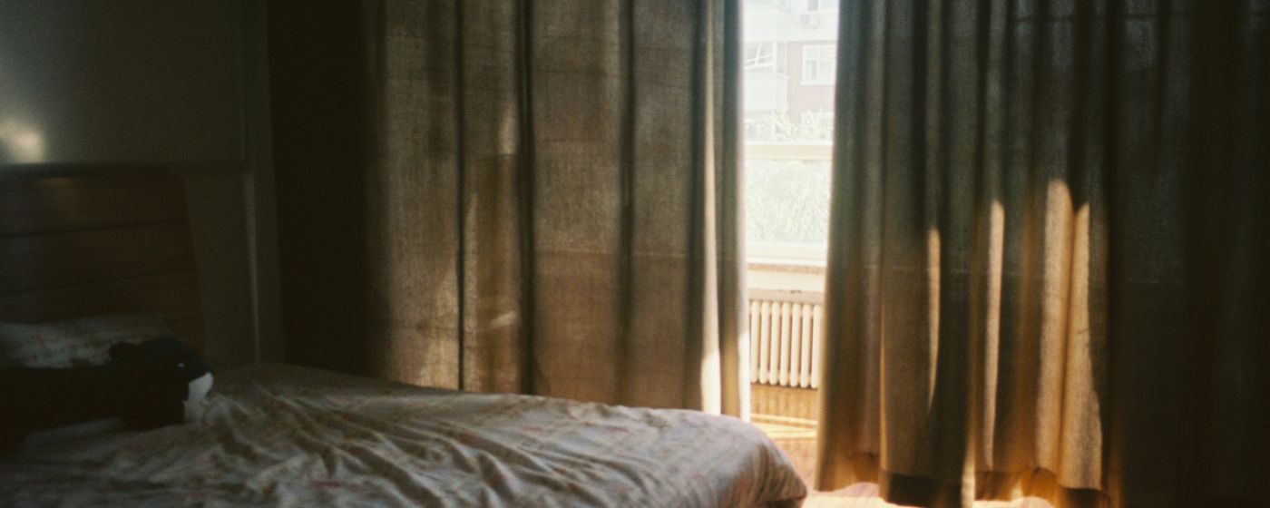 Early morning light coming through curtains onto an unmade bed