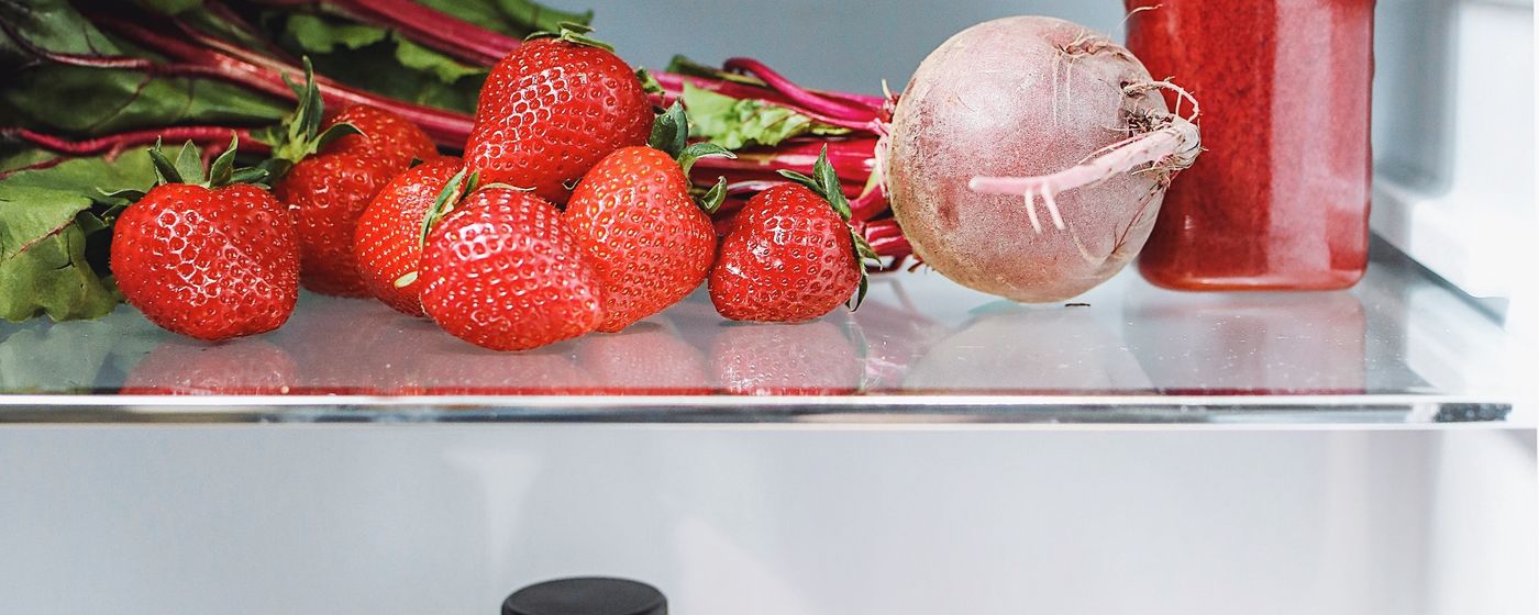 Fresh strawberries and a beet on a refrigerator shelf