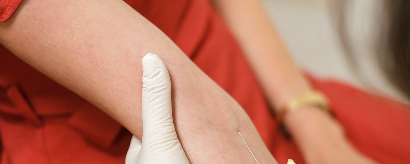 A gloved hand drawing blood from the inside of a person's arm with a fine needle