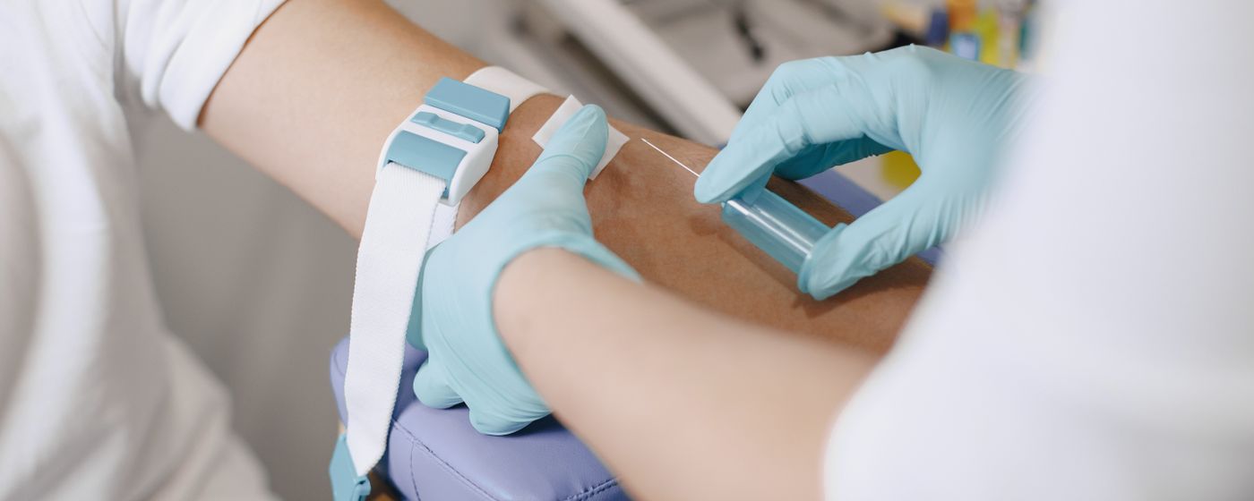 A gloved hand drawing blood from a person's arm with a tourniquet in place