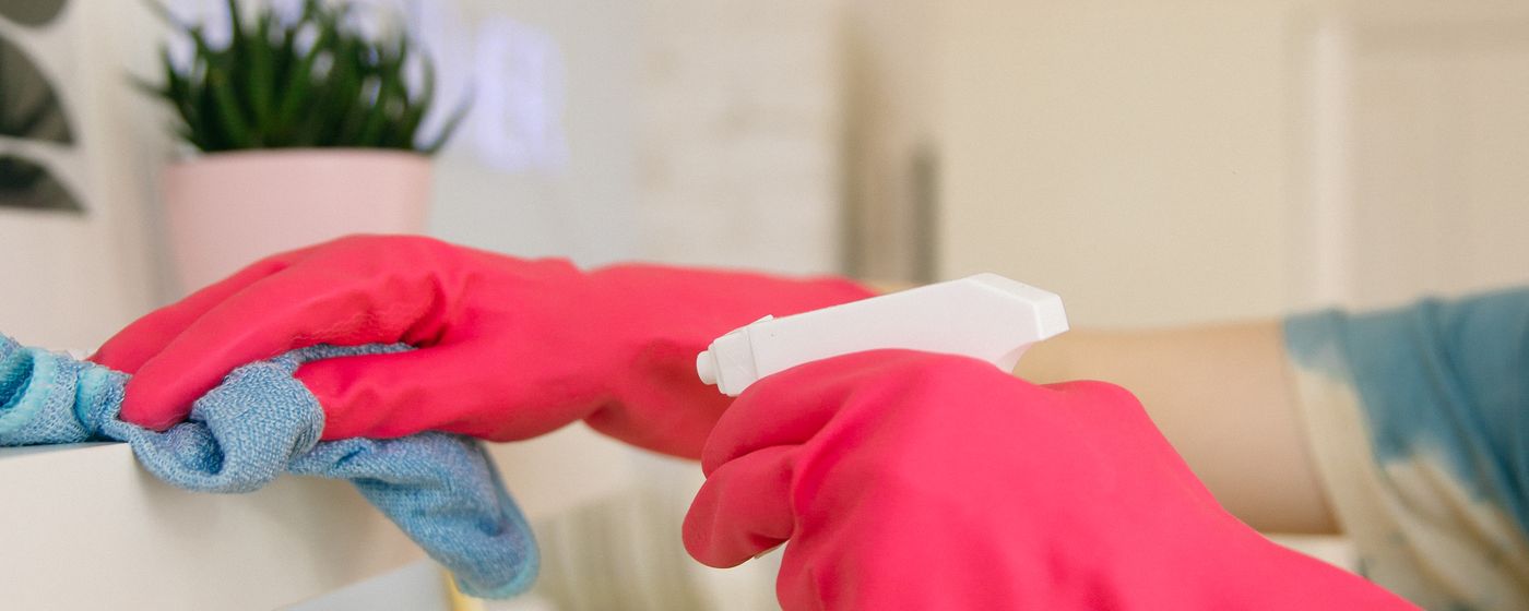 A gloved hand wiping a kitchen surface with a cloth beside a spray bottle