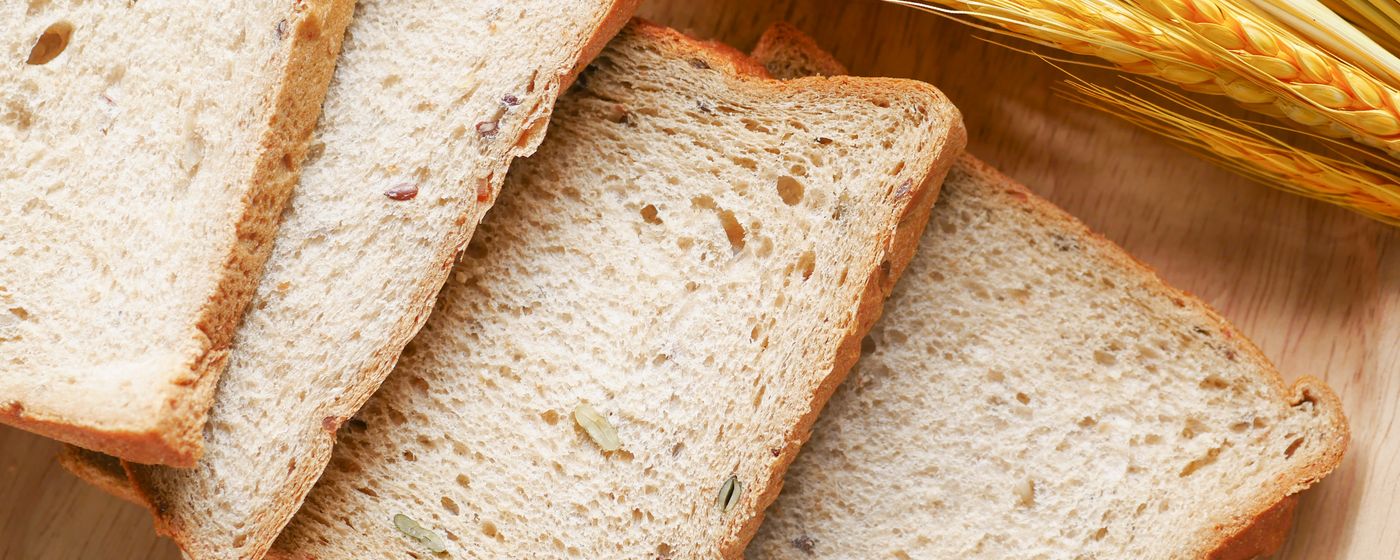 Slices of bread on a wooden board beside ears of wheat