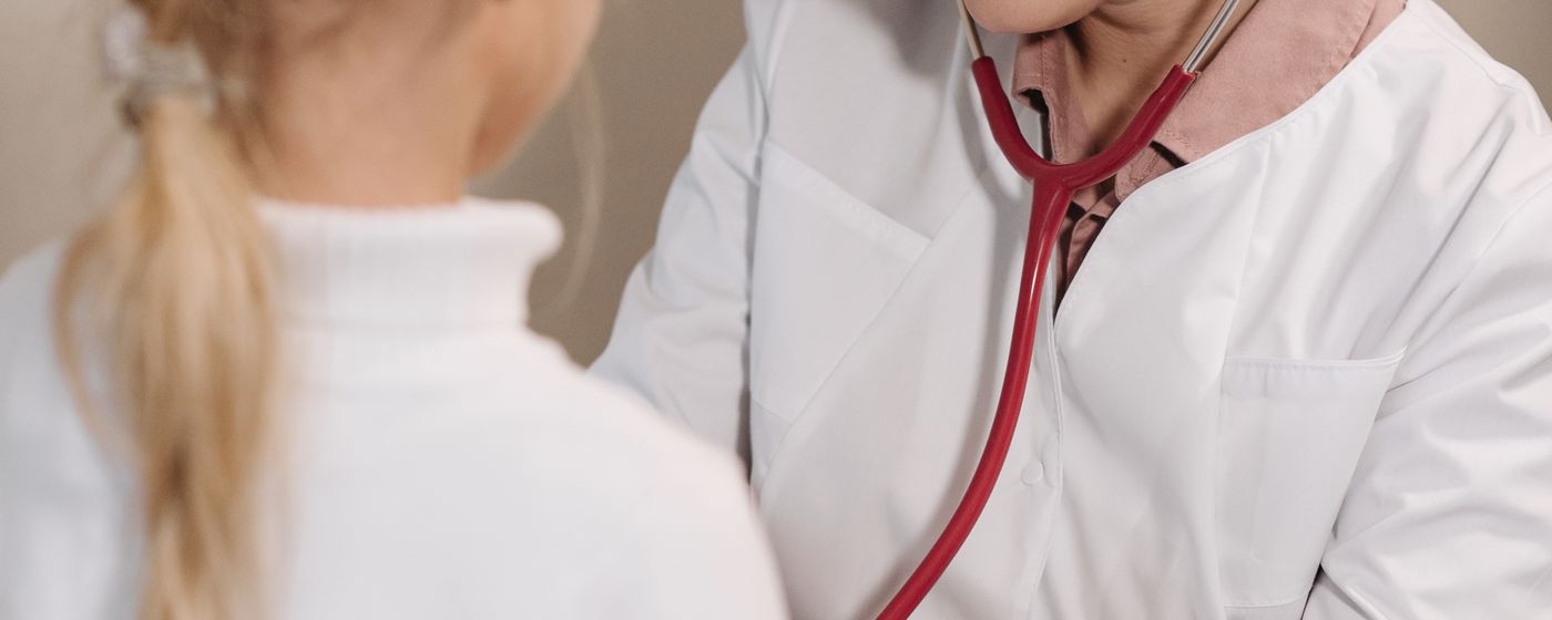 A clinician in a white coat listening to a patient's chest with a stethoscope