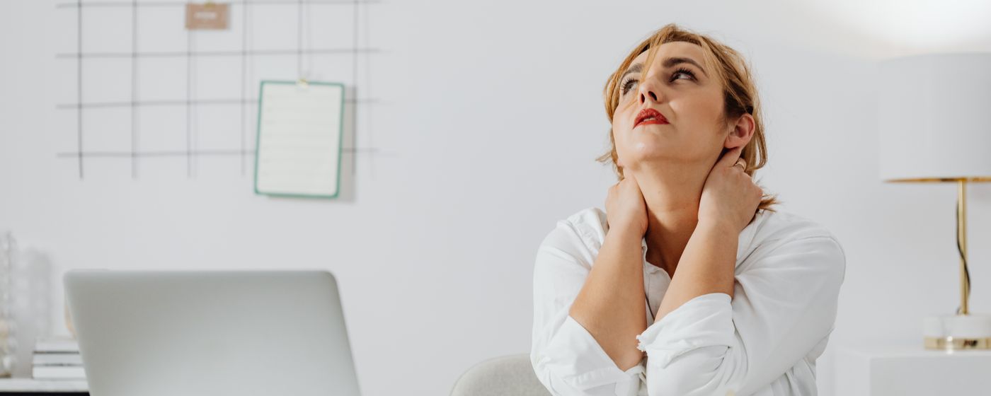 A woman at a desk with a laptop holding the back of her neck