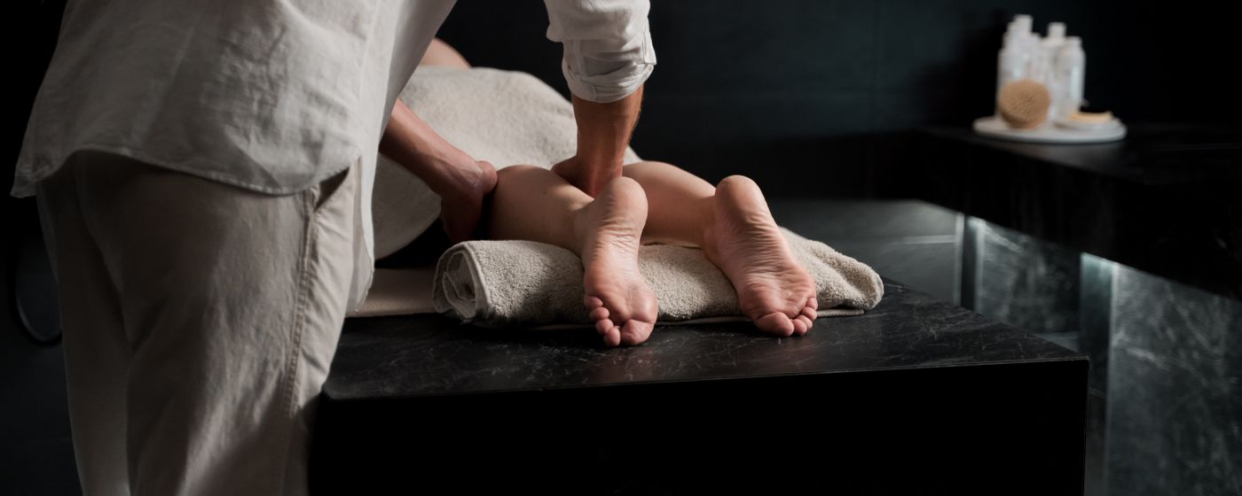 A therapist massaging a person's lower legs and feet on a treatment table
