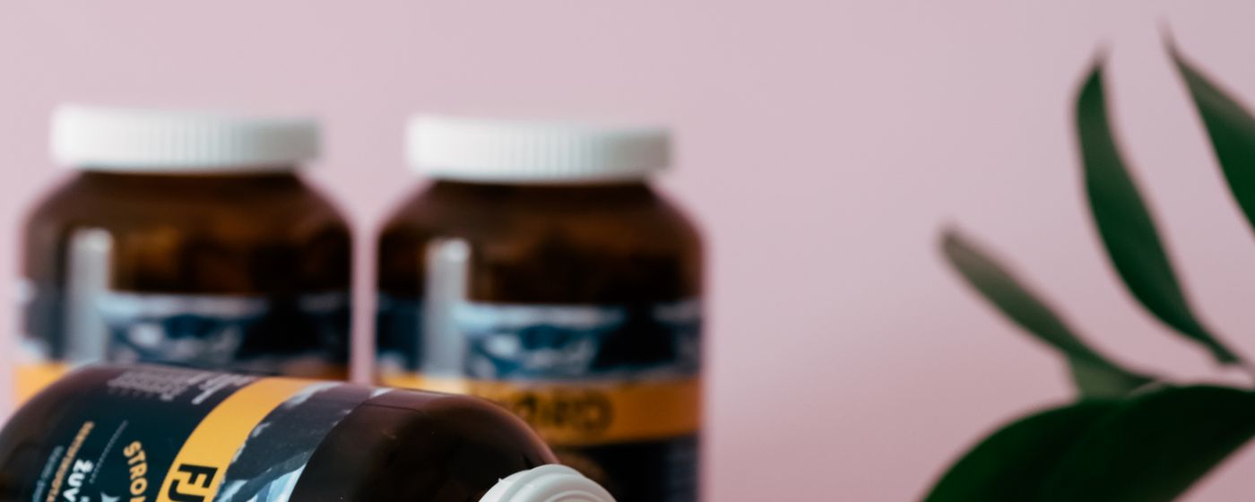 Two amber supplement bottles standing on a pink surface beside a green plant leaf