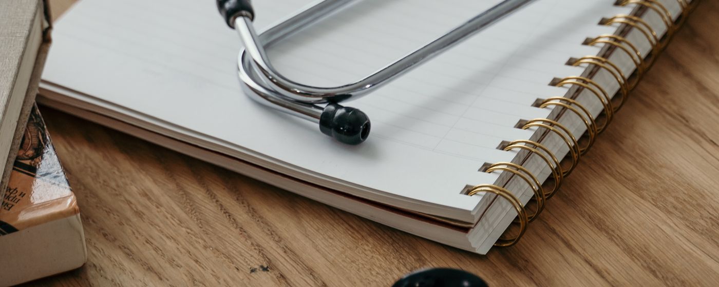 A stethoscope resting on a spiral bound notebook on a wooden desk