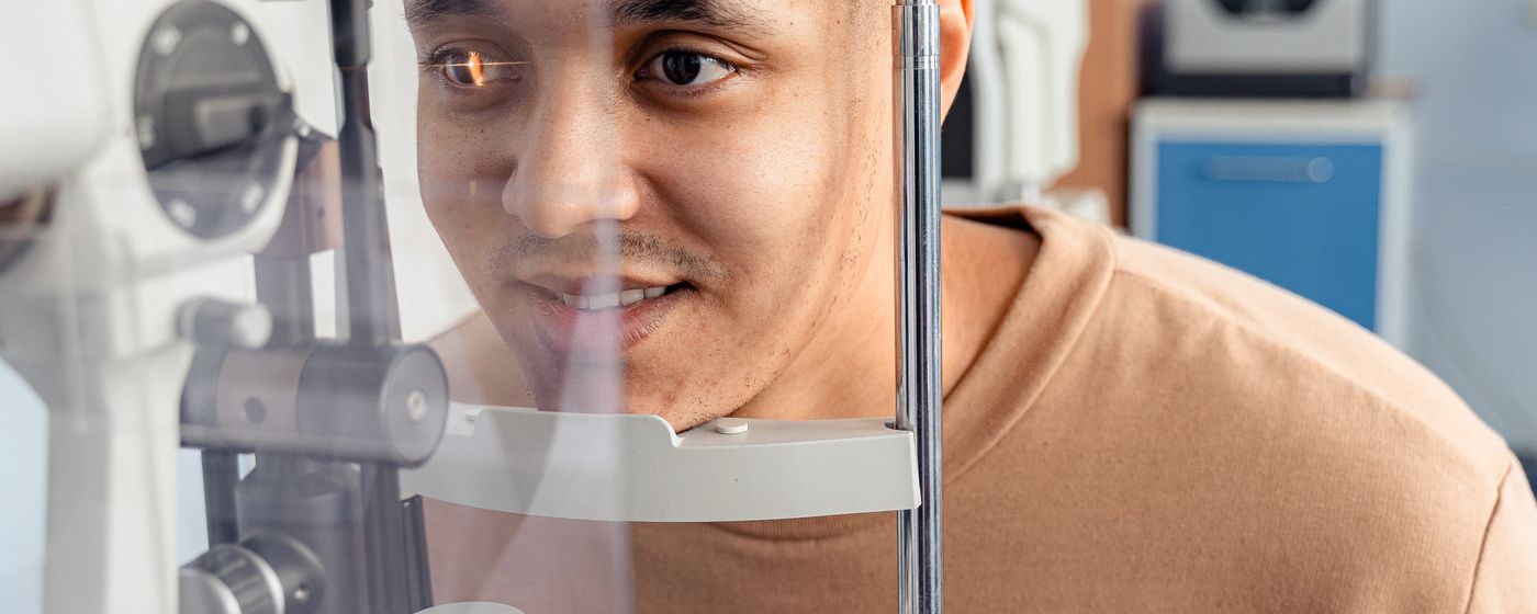 A man resting his chin on an eye examination machine while a clinician checks his eyes