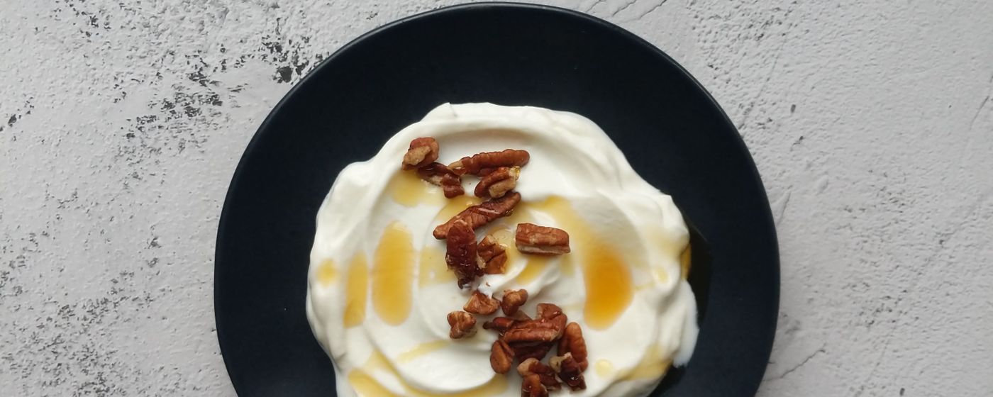 A bowl of plain yogurt topped with honey and pecans on a grey stone surface