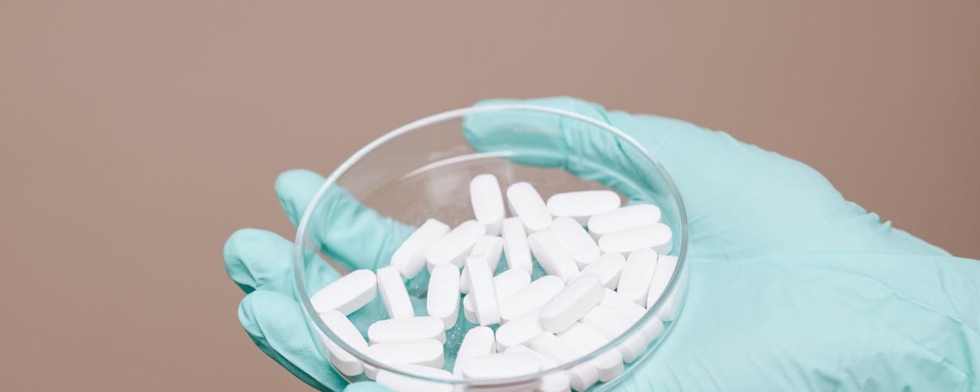 A gloved hand holding a glass dish filled with white capsules