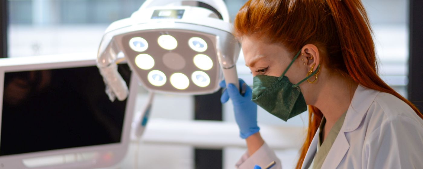 A dental clinician in a mask adjusting an overhead light in a treatment room