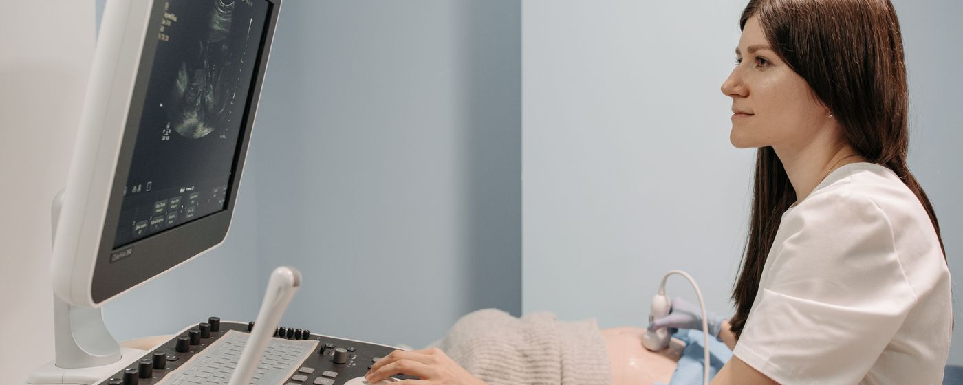 A sonographer working at an ultrasound machine beside a patient lying on the examination bed