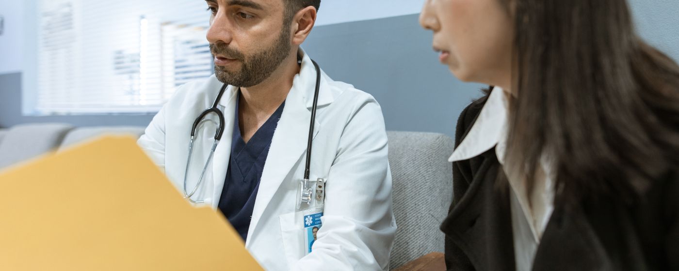 A doctor in a white coat talking with a patient across a desk