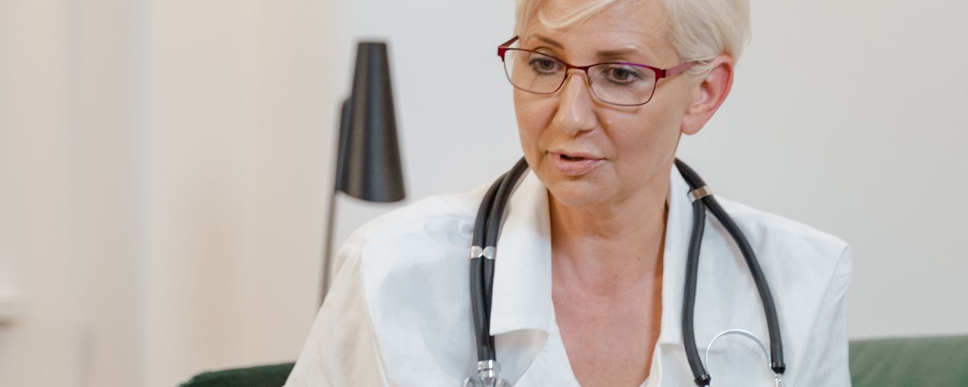 A physician in a white coat with a stethoscope looking down at notes in a clinic room