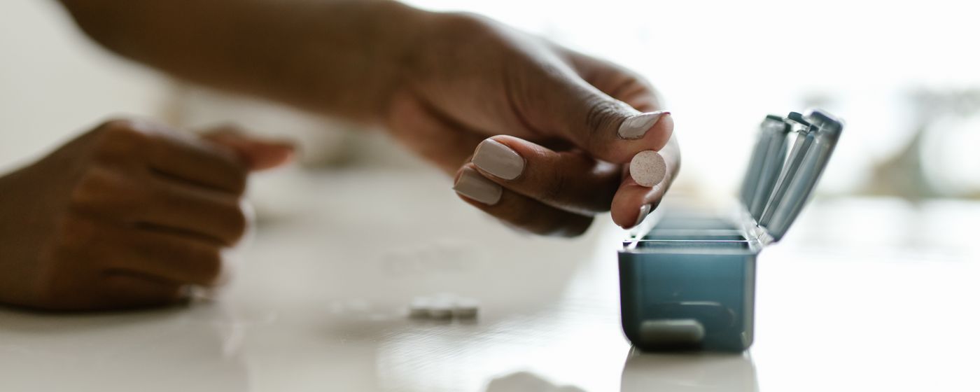 Hands sorting tablets into the compartments of a weekly pill organizer on a table