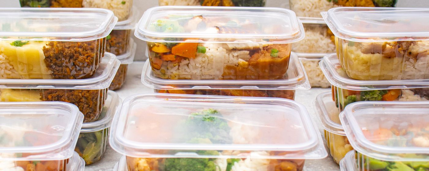 Rows of shallow clear plastic containers filled with cooked chicken, rice and vegetables