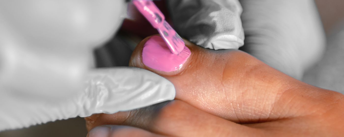 A gloved hand filing the surface of a person's toenail during a foot care appointment