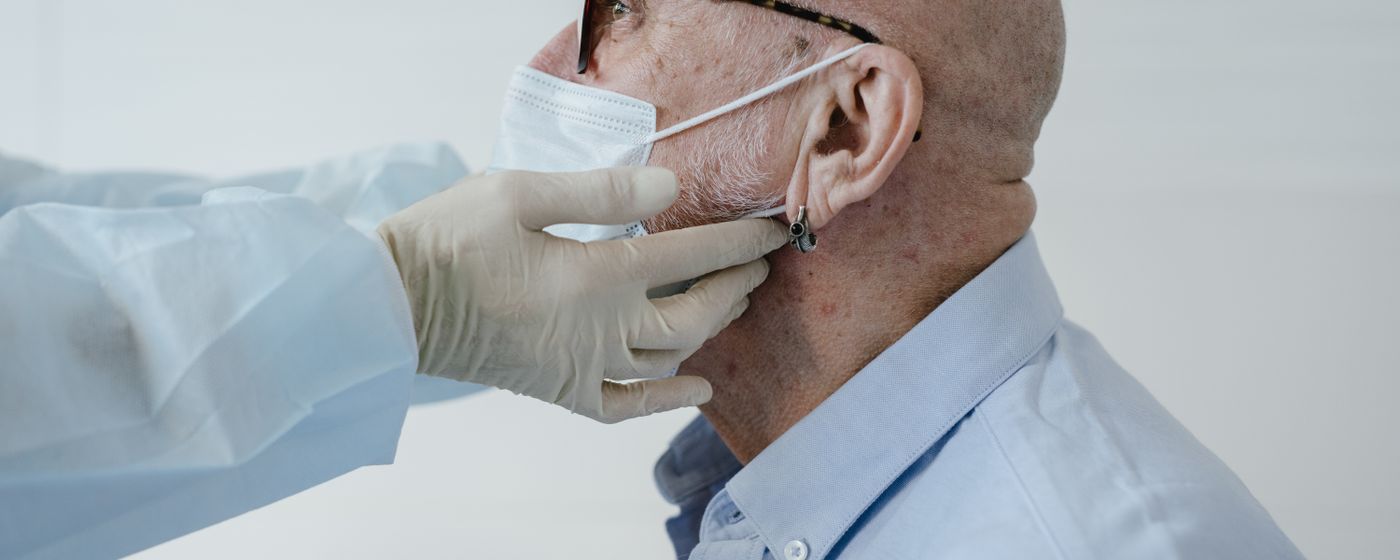 A clinician wearing gloves examining an older man's neck during a medical appointment