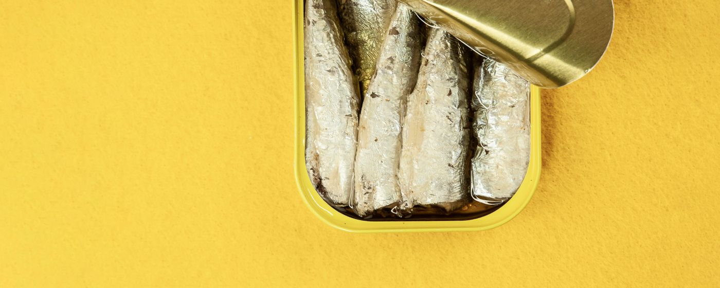 An open tin of sardines in oil on a bright yellow background