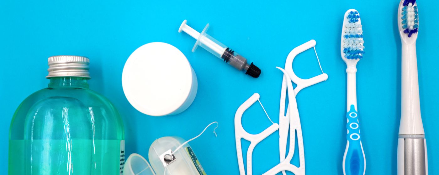 A mouthwash bottle, floss picks and toothbrushes arranged on a bright blue surface