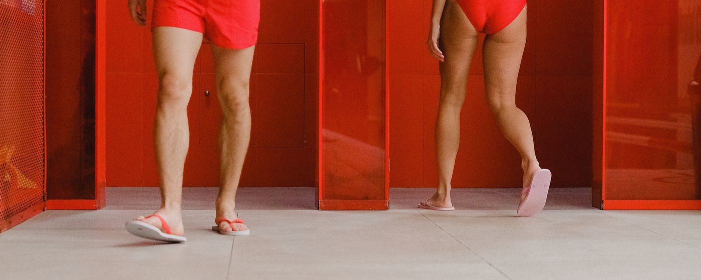 Two people wearing flip flops standing on the tiled floor of a locker room