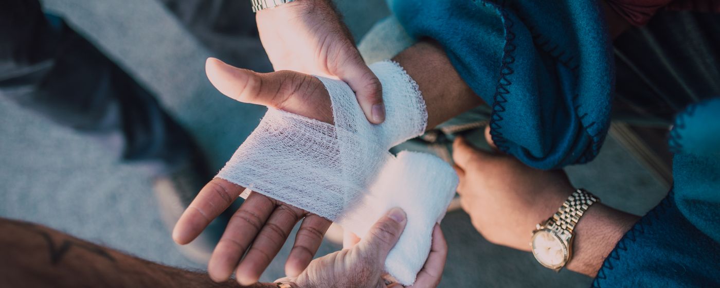 One person wrapping a white elastic bandage around another person's hand and wrist at a table