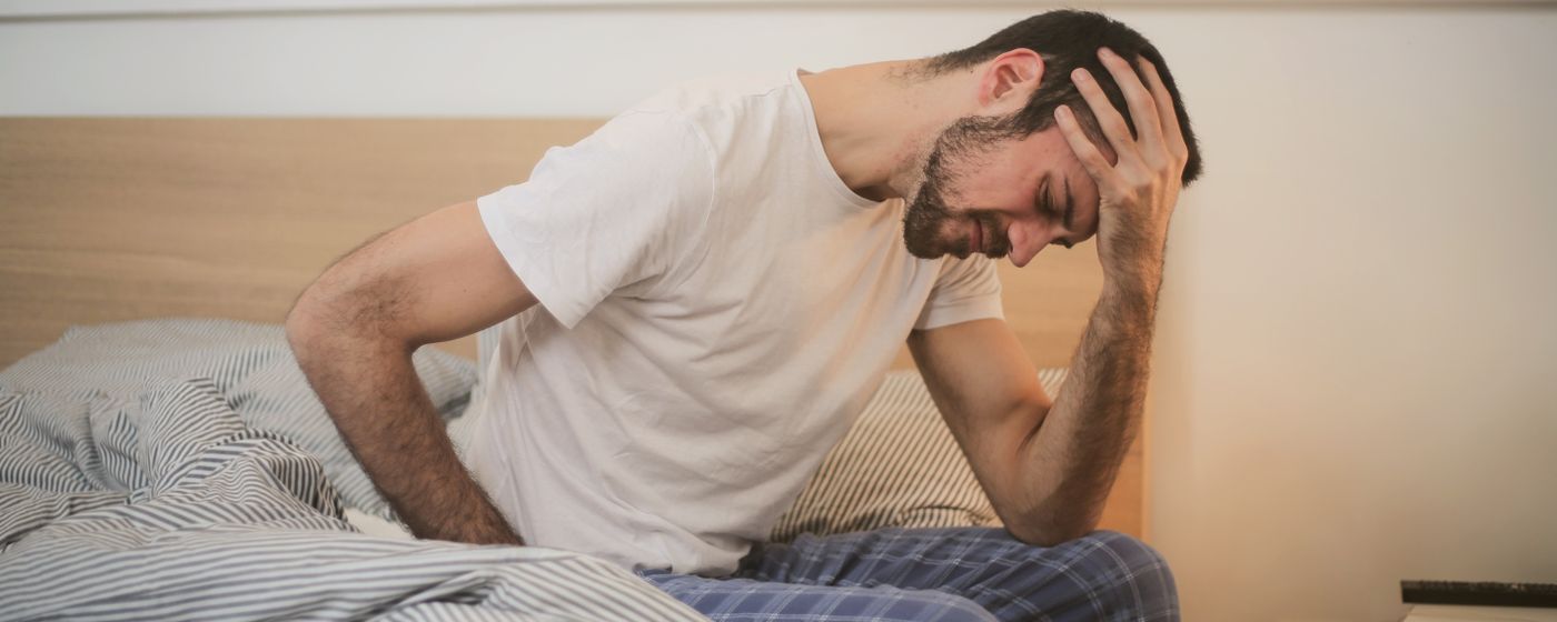 A man sitting on the edge of a bed in the morning with his head in his hand