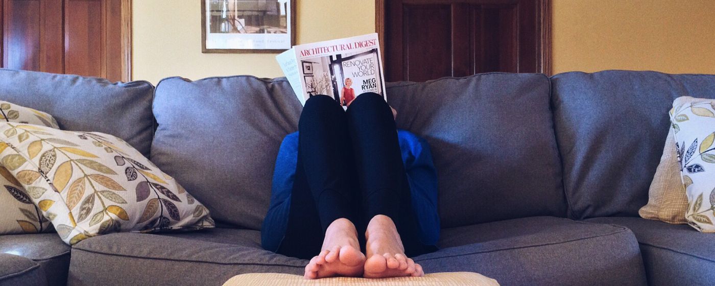 Person sitting on a couch with legs stretched out and bare feet resting on an ottoman