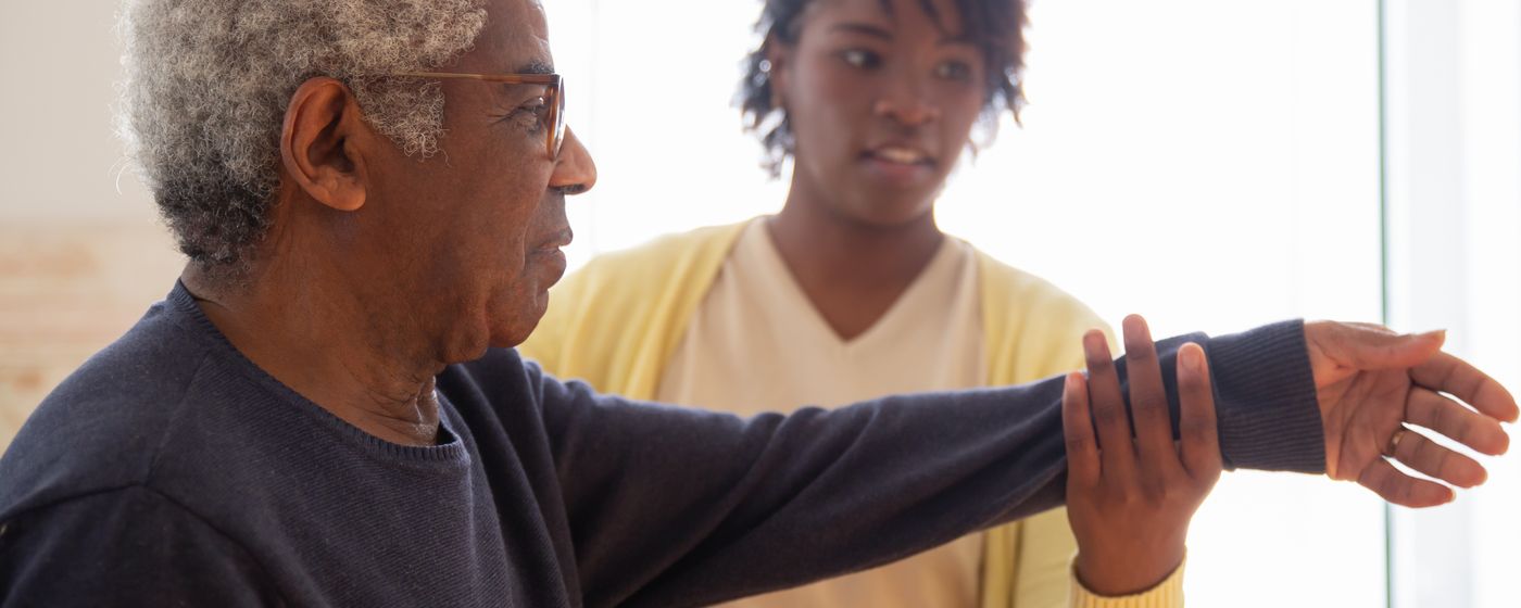 A caregiver guiding an older man's outstretched arm through a stretching exercise