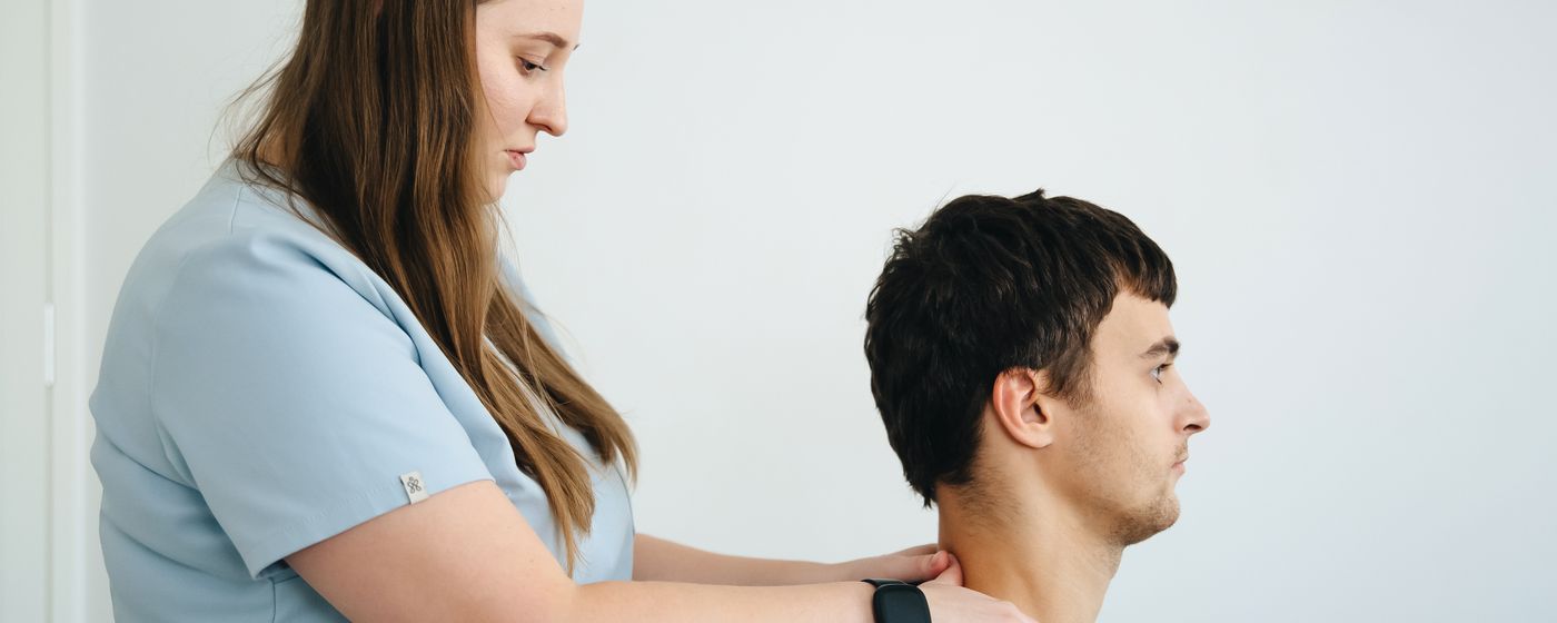 A clinician standing behind a seated patient with both hands supporting the head and neck
