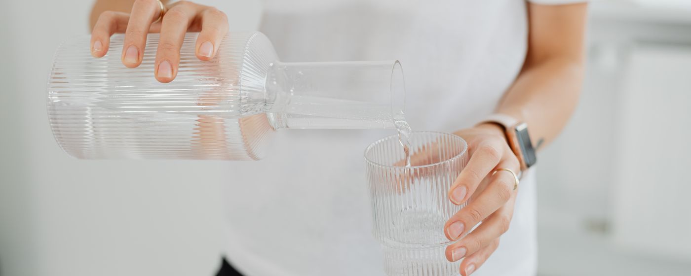 A person pouring water from a glass carafe into a drinking glass on a kitchen counter