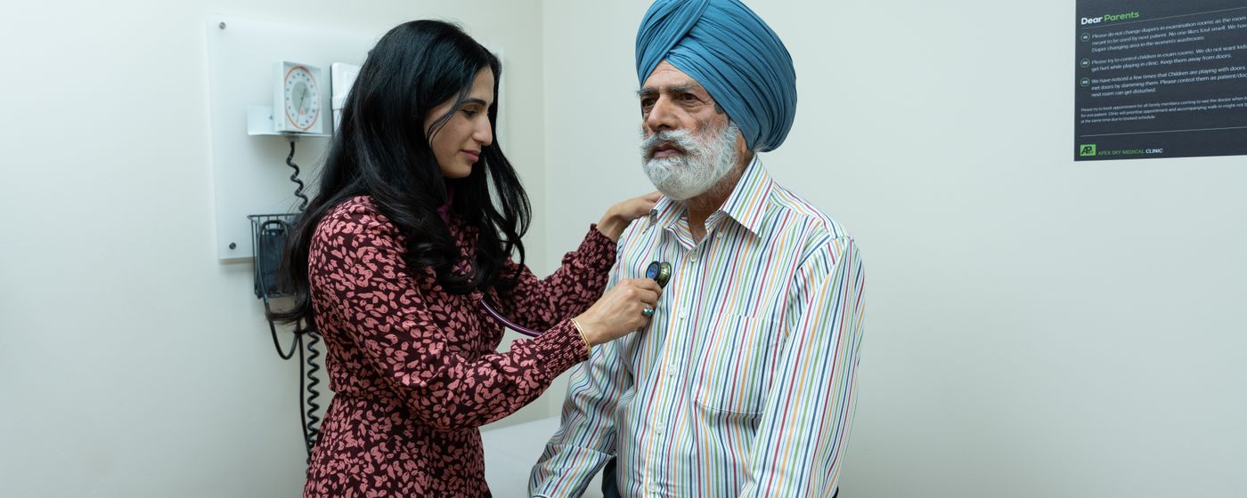 A doctor uses a stethoscope to examine a senior man in an exam room