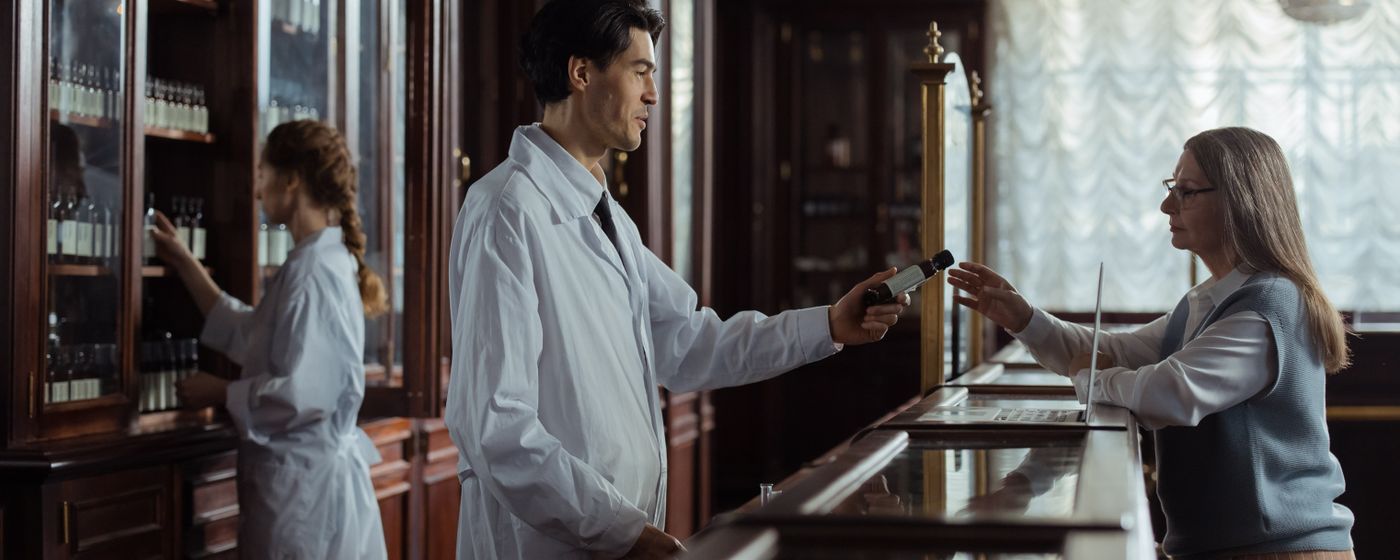 A pharmacist hands medication to a customer across a pharmacy counter