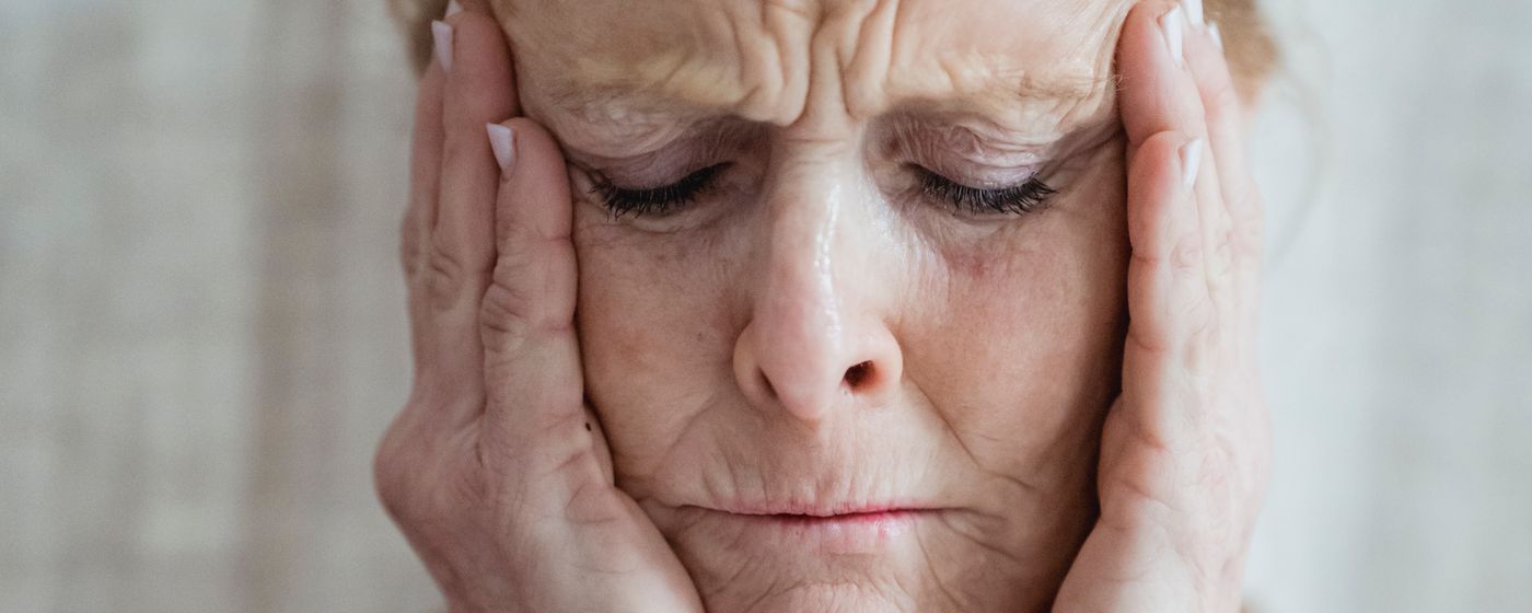 A senior woman with eyes closed pressing her hands to her temples at home