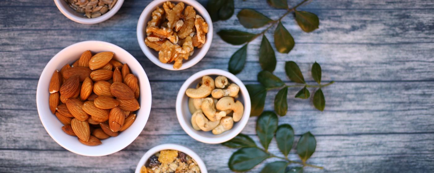 Almonds, walnuts and cashews in small white bowls on a blue wooden table