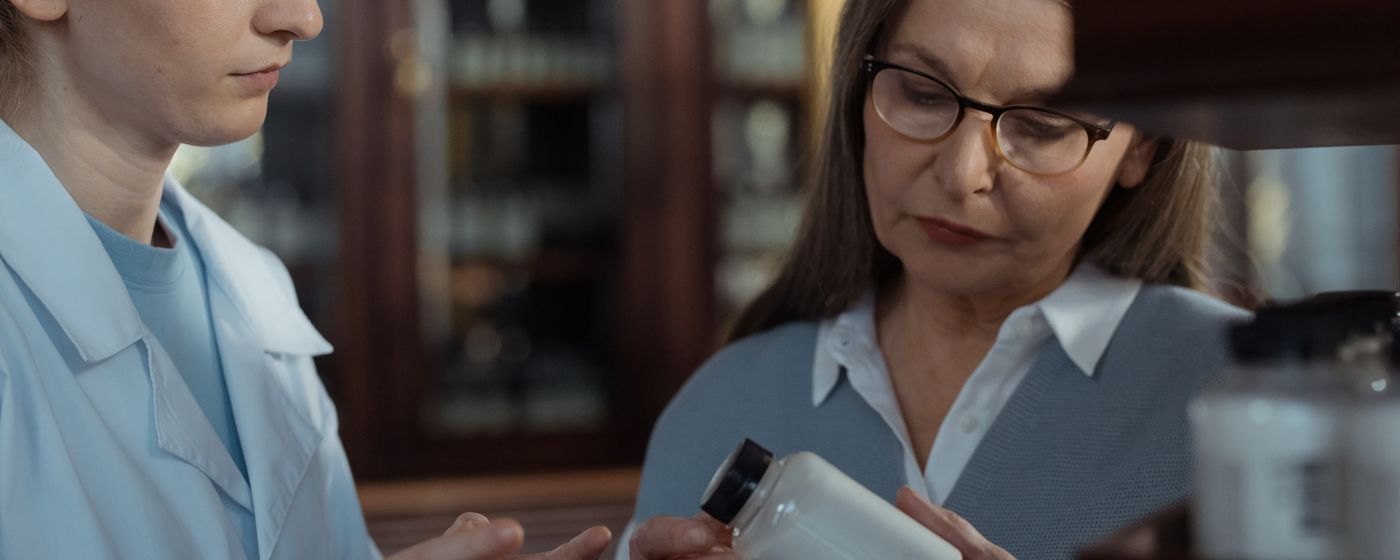 A pharmacist discussing a medicine box with an older woman at a pharmacy counter