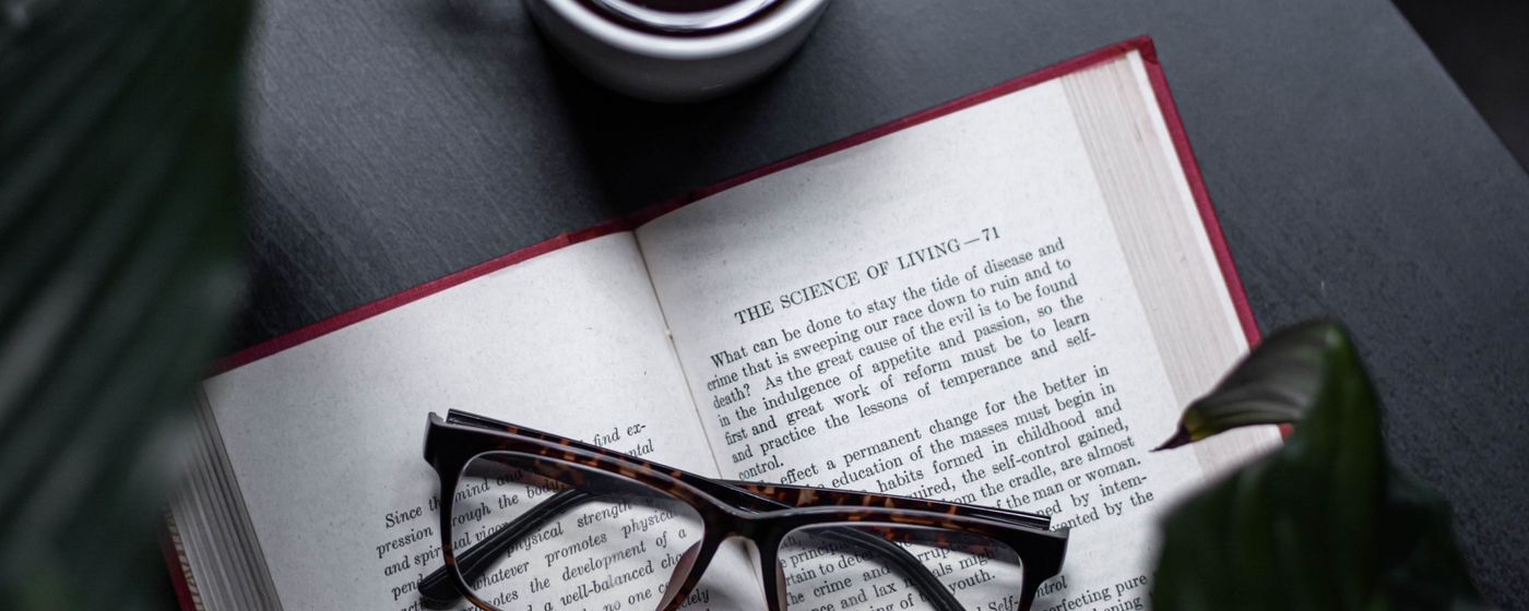 Reading glasses resting on an open book beside a cup of coffee